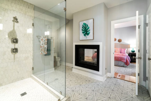 black and white pattern tile floor in bathroom with shower and fireplace looking into bedroom